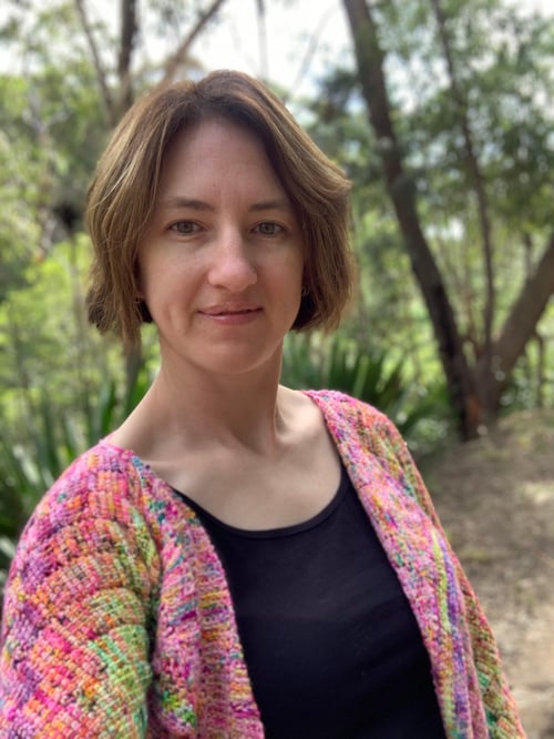 white brunette woman wearing a Tunisian crochet cardigan and black t'shirt standing in the Australian bush