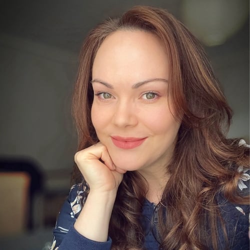 Smiling woman with long wavy hair, wearing a navy top with floral details, resting her chin on her hand in a relaxed and friendly pose. This is Caroline Bauer, registered nutritionist and creator of Add2Eat—a habit-based approach to healing your relationship with food.