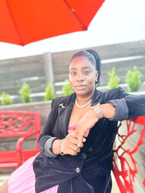 TaKeisha Brown, founder of Monarch Kreationz, seated confidently under a vibrant red umbrella embodying divine purpose, elegance, and creative leadership.
