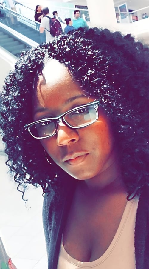 Black female author with curly hair and glasses, looking confident in natural light — founder of Pages & Power, storyteller, entrepreneur.”
