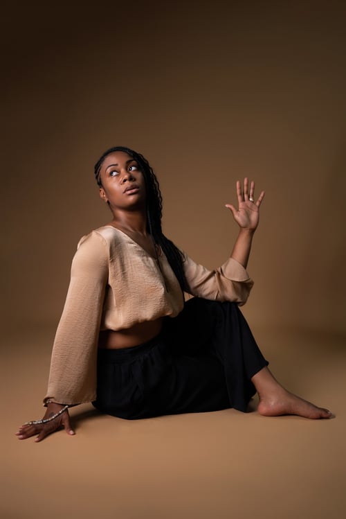 Kaysha — professeure de yoga et future instructrice Pilates, en posture assise ancrée, expression de puissance et sérénité, dans un studio à lumière dorée.