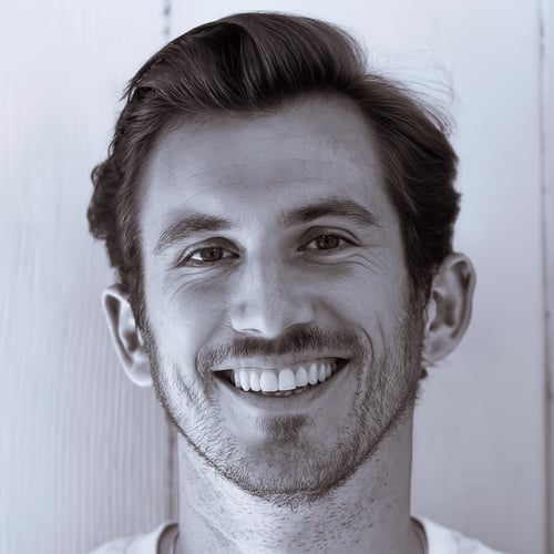 Portrait of Pedro Lara, a contemporary digital artist based in Mallorca, Spain. He stands against a light wooden background, wearing a light-colored shirt and styled short hair. The image conveys a clean, modern aesthetic aligned with his creative identity. Ideal for representing a professional visual artist in the digital space.