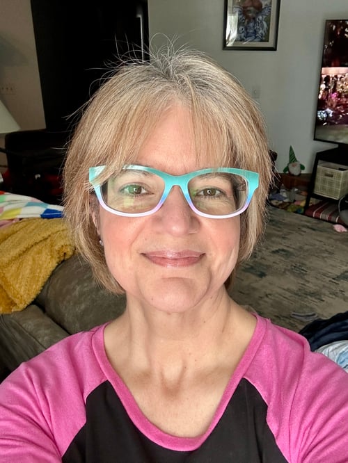 Profile picture of Angelina Potter. Blondish hair, brightly colored glasses wearing a black and pink shirt.