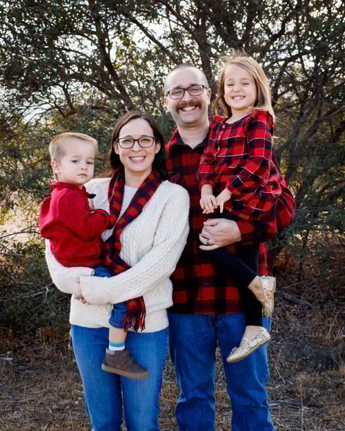Laura Legge standing outdoors with her husband and two children, smiling together in coordinated red and neutral outfits.