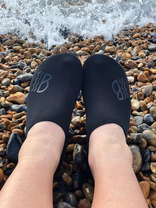 Black water shoes on a person's feet on a stony beach