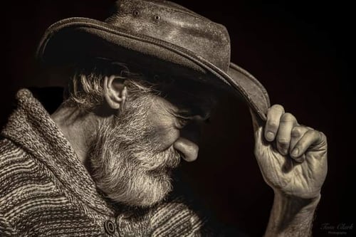 Side profile in cow boy hat with beard with hand tipping the brim