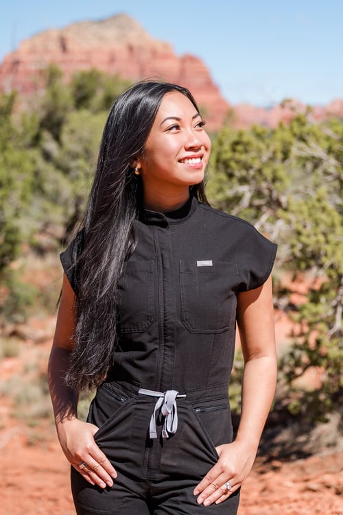 Professional portrait of a smiling woman wearing black scrubs outdoors, surrounded by desert greenery and red rock scenery.