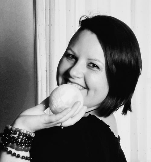 Photograph of Evylyn Rose in black and white. She is smiling with joy and holding a selenite sphere that appears like a small moon. Her wrist is adorned with several crystal bracelets. Photograph by Matanda Mondoa.