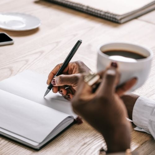 Woman writing in a journal while enjoying her morning coffee