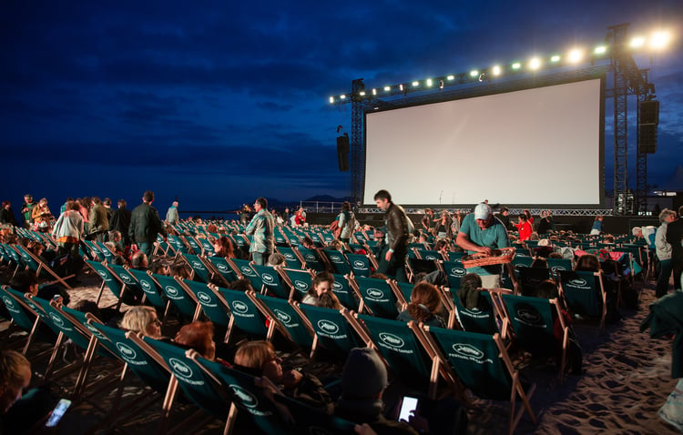 A large outdoor movie screen and people to watch the show.