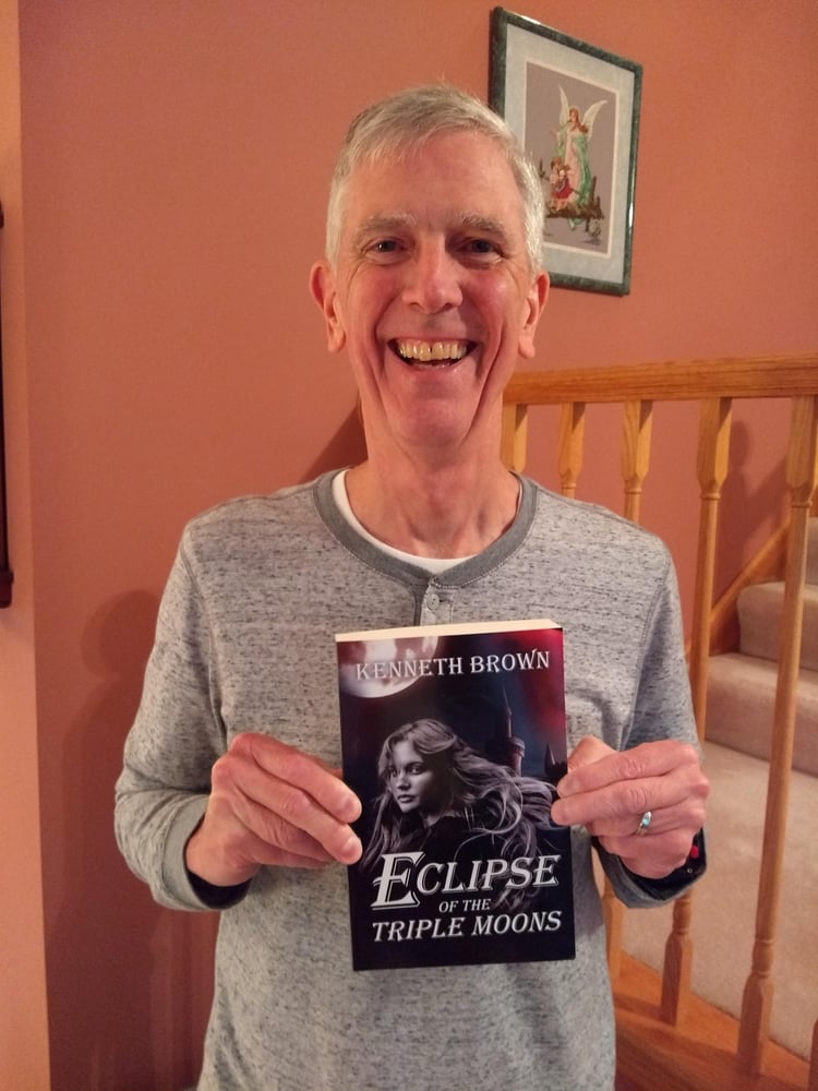 Kenneth Brown Author Holding the paperback version of Eclipse of the Triple Moons
