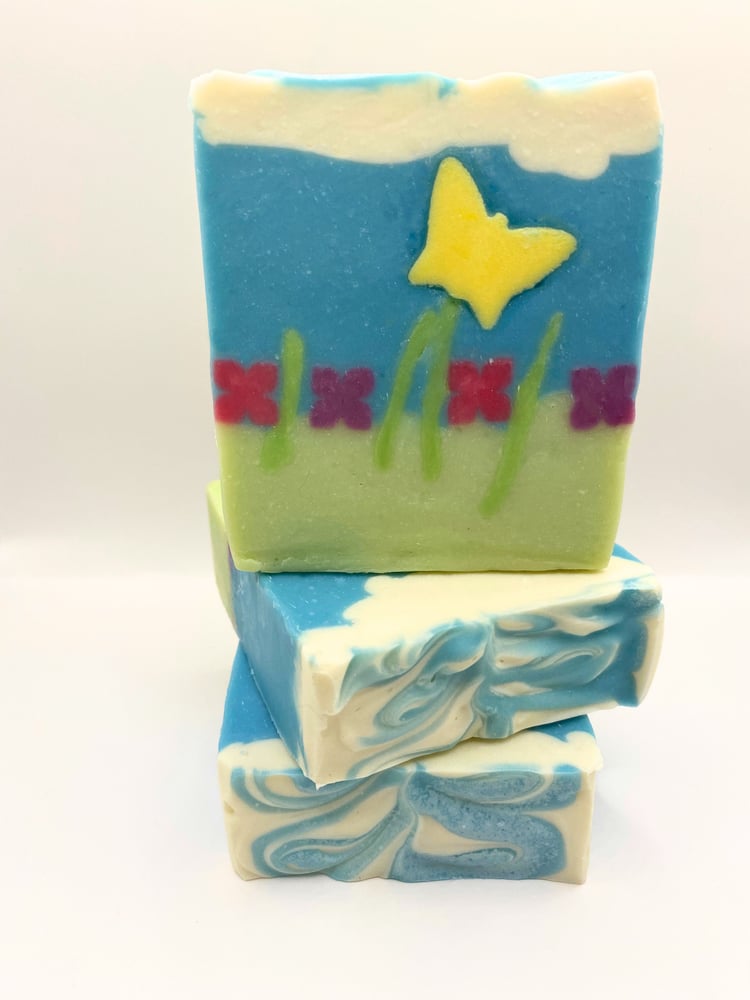 Bars of handmade soap featuring a butterfly flittering across a meadow of flowers under a blue sky topped with puffy white clouds
