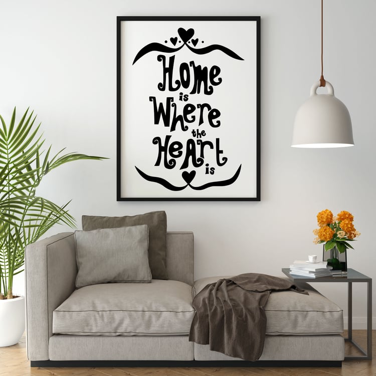 A large print featuring the phrase "Home is Where the Heart is" hung behind a grey sofa.