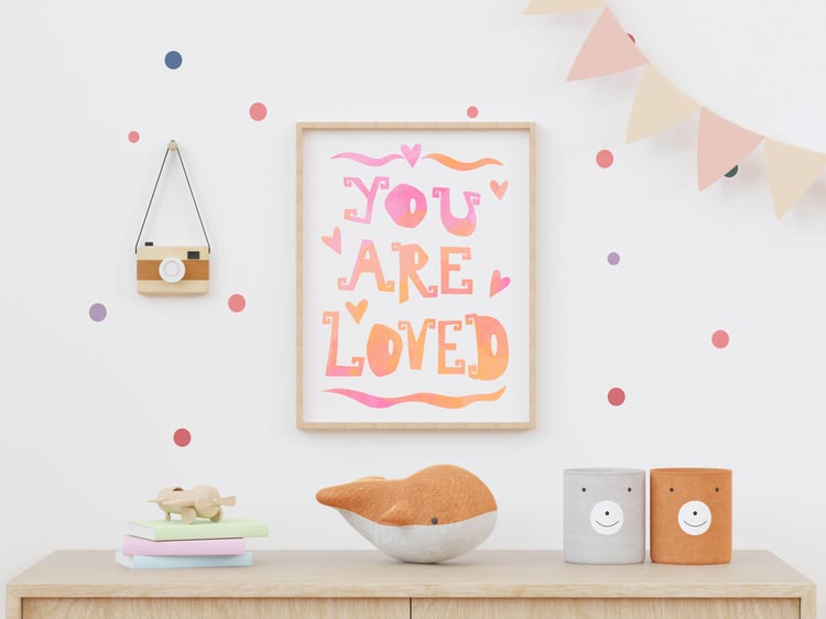 "you Are Loved" print, hung on a nursery wall surrounded by toys.