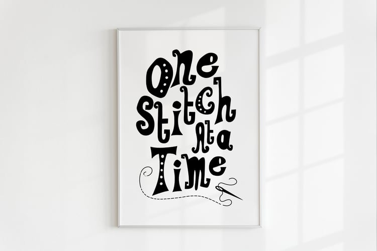 A downloadable print with a hand lettered design which says ‘one stitch at a time’ in black.