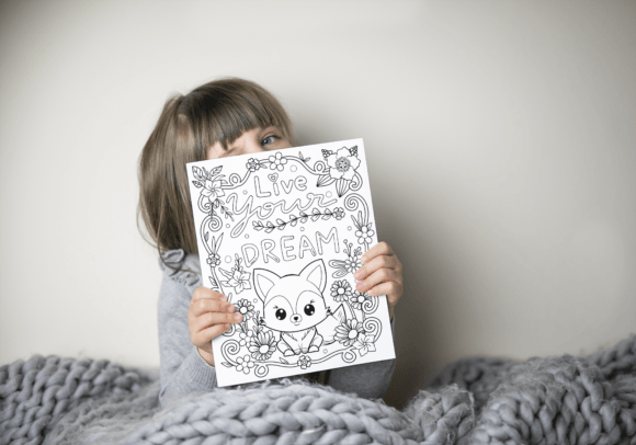 A child sits under a cozy grey blanket, holding a coloring page featuring a cute fox and the word "DREAM" surrounded by flowers.