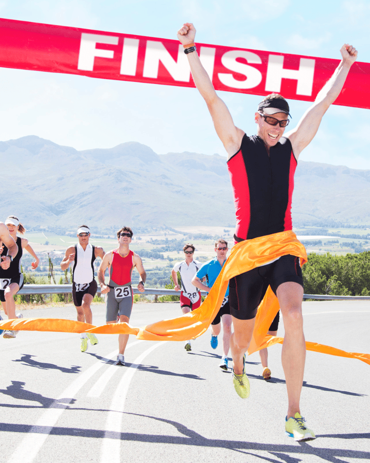A group of men over 40 crossing the finish line of a race, raising their arms in triumph. Their faces show determination, relief, and accomplishment, symbolizing perseverance, commitment, and the rewards of pushing through physical and mental challenges
