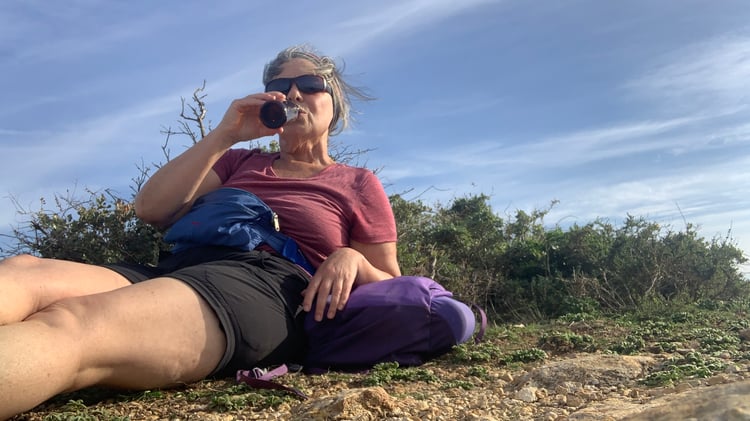 Female hiker drinking a beer with dysphagia after a long hot hike. Looking out over the sea.