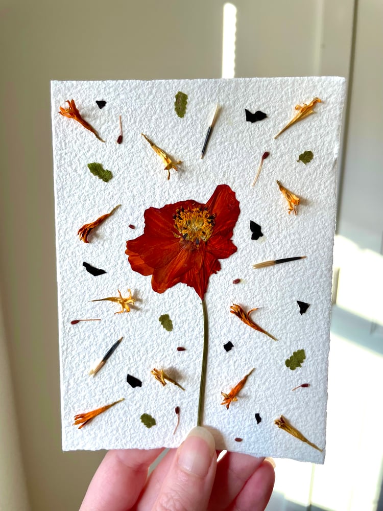 A hand holding a card made with pressed flowers