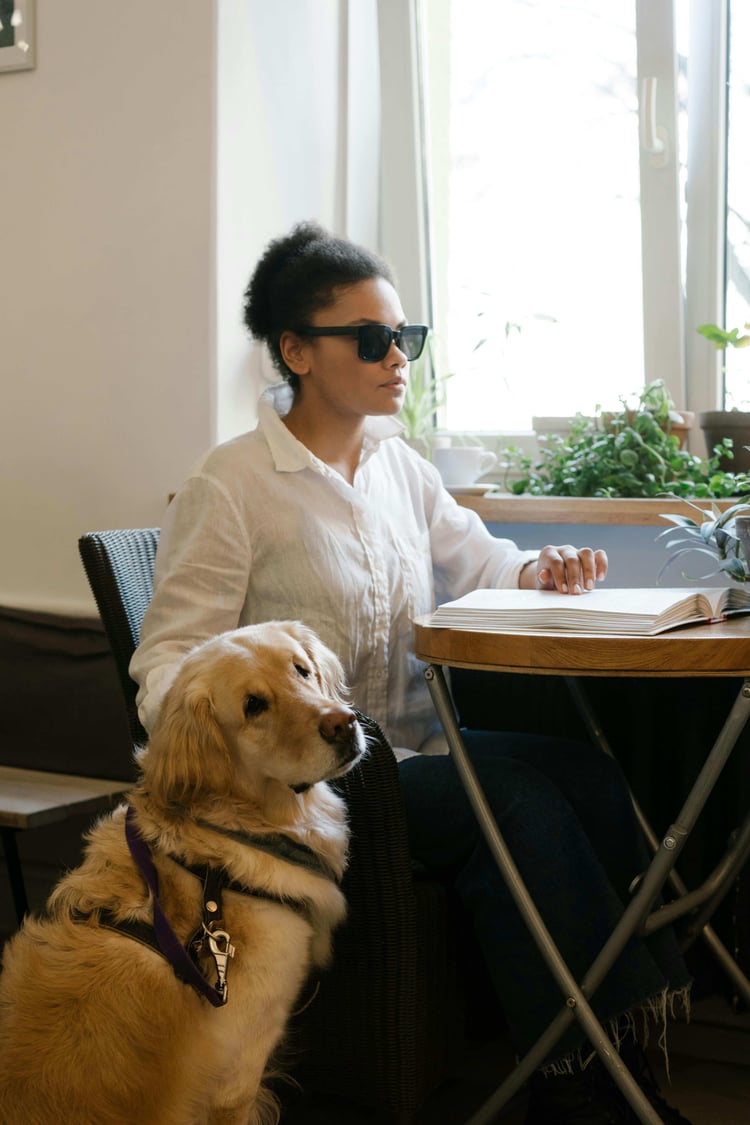 a blind black woman reading braille next to her service guide dog