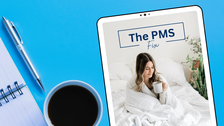 A relaxed young woman sits on a cozy white bed, wrapped in a soft blanket, holding a warm mug. Above her, the text "The PMS Fix" is displayed in a stylish blue font. She is happy she no longer has PMS symptoms.