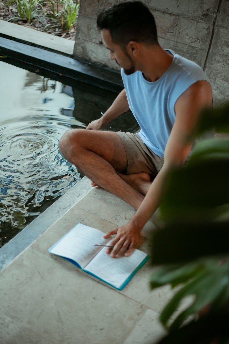 Yoga Teacher Tristan writing in a notebook and looking at ripples in water