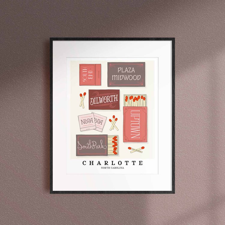 A framed picture of Charlotte, North Carolina neighborhoods drawn in various lettering styles on matchboxes. Artwork has a pink, grey and burgundy color scheme.