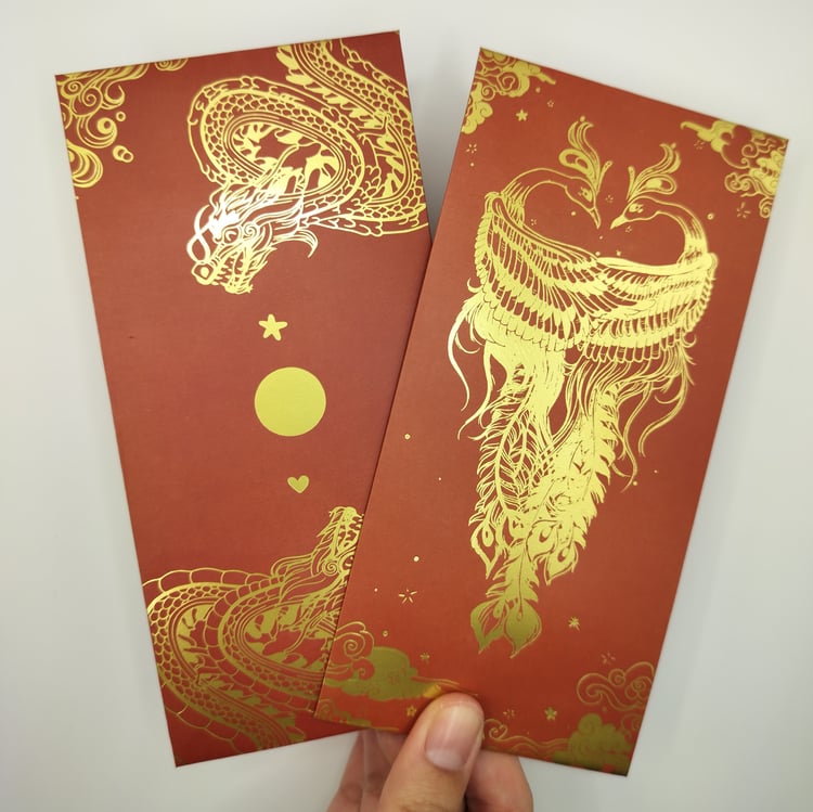Hand holding two red hongbaos with gold foil designs - one featuring dragons with decorative elements like stars and circles, and another with an two phoenixes surrounded by clouds and ornamental details.