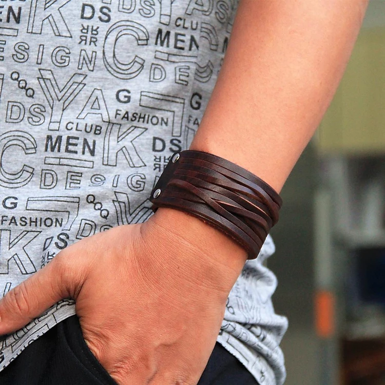 Man wearing a dark brown Vintage Two Layers Wide Leather Cuff Bracelet (Product ID: jf86182040) on his wrist. This punk-style bangle wristband features multiple overlapping straps and is styled with a grey graphic print sleeveless top.