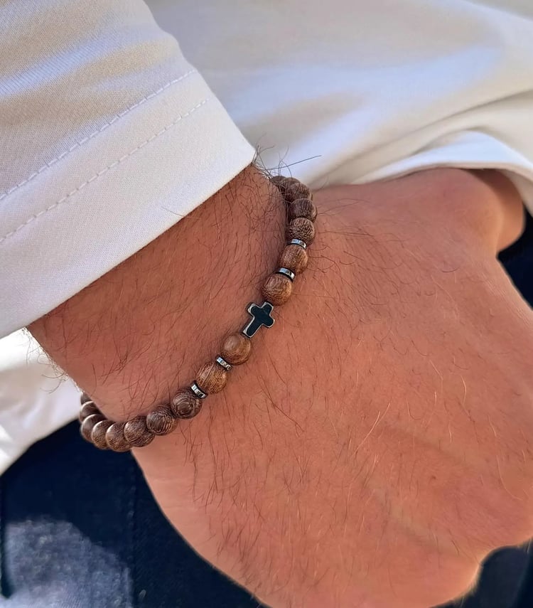 Natural wood bead stretch bracelet featuring round brown beads with dark grain, a central dark grey metallic cross charm, and faceted hematite spacer beads. Ideal Christian or religious mens jewelry.