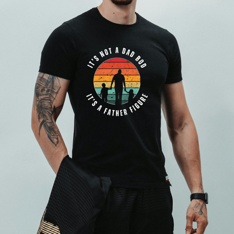 Casual man modeling a black t-shirt with a colorful vintage-style graphic and “It’s Not a Dad Bod It’s a Father Figure” phrase across the chest.