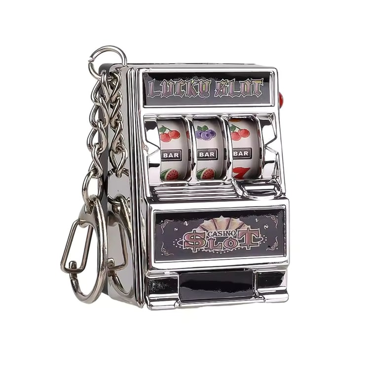 Product shot of a chrome-finish miniature slot machine keychain with black accents. The stationary reels display classic fruit machine symbols including cherries, blueberries, and the BAR symbol. The novelty keyring has a working side lever and a durable