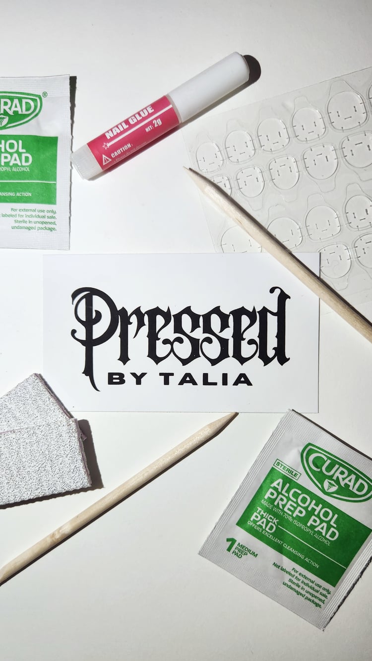 Picture of press-on nail prep and application kit containing: wooden cuticle pushers, a tube of nail glue, a sheet of nail adhesive tabs, two mini nail buffers, and two alcohol prep pads