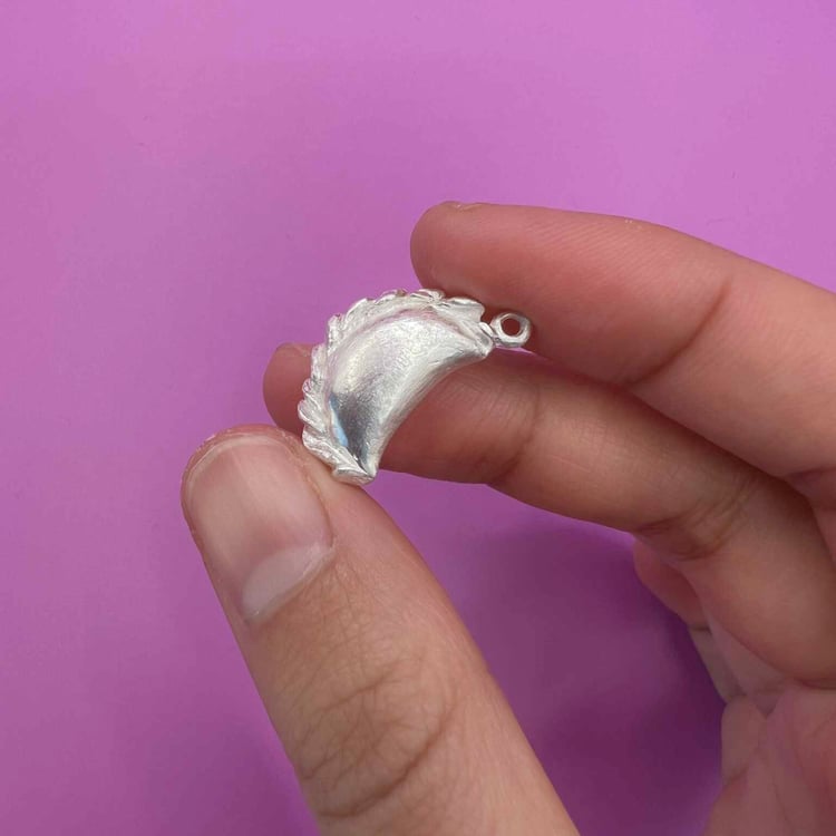 Silver curry puff pendant held over a bright fuschia background