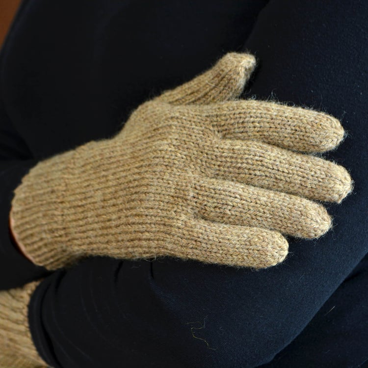 A simple knit glove in beige worsted weight yarn being modelled by a woman with size large hands. Glove has a plain stockinette body, long ribbed cuff, and a thumb gusset.