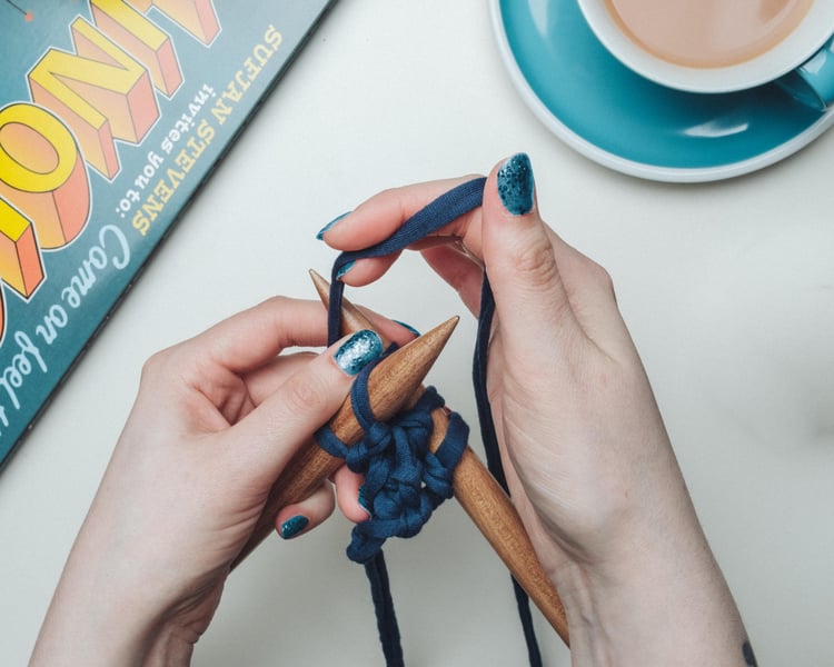A woman's hands work a knit stitch on chunky needles.