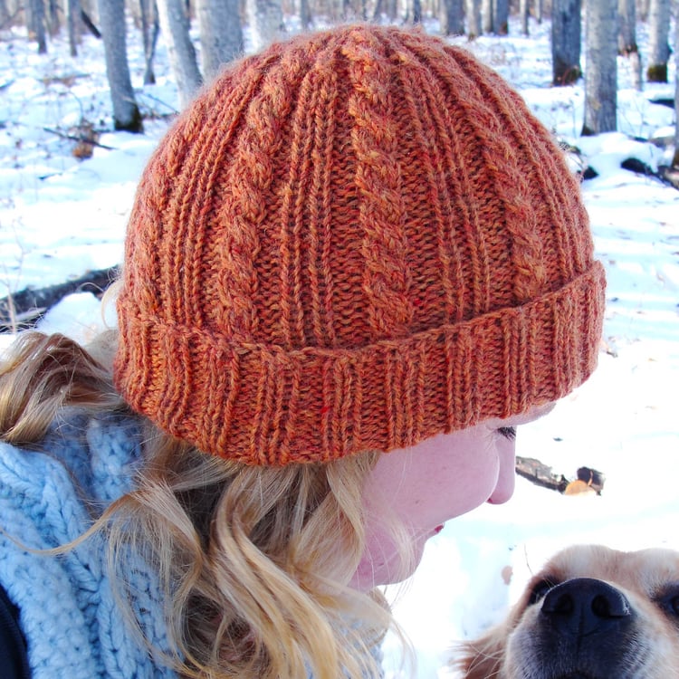 Profile of a woman wearing a Brennan Hat cable-knit beanie with a rolled 2x2 ribbed brim looking down at her dog, a golden retriever.