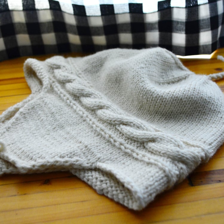 Flat lay of cream Twisted Rope Hat in Size 6 - Adult Medium, with angular ear flaps and tassels.