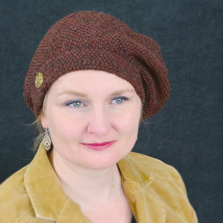 Woman wears rich brown beret with gold military-looking button on the hatband, and the hat slouching to the other side.