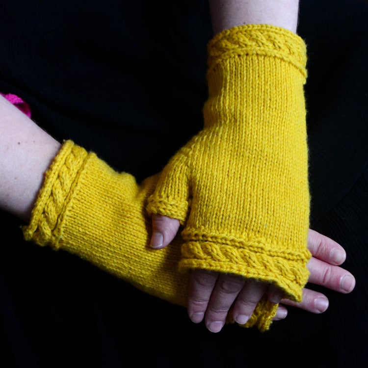 Close-up of crossed hands wearing golden Twisted Rope Fingerless Mittens against a black background.