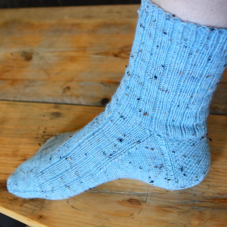 Womans foot wearing a tweedy light blue ribbed sock with the heel flap and gusset visible.