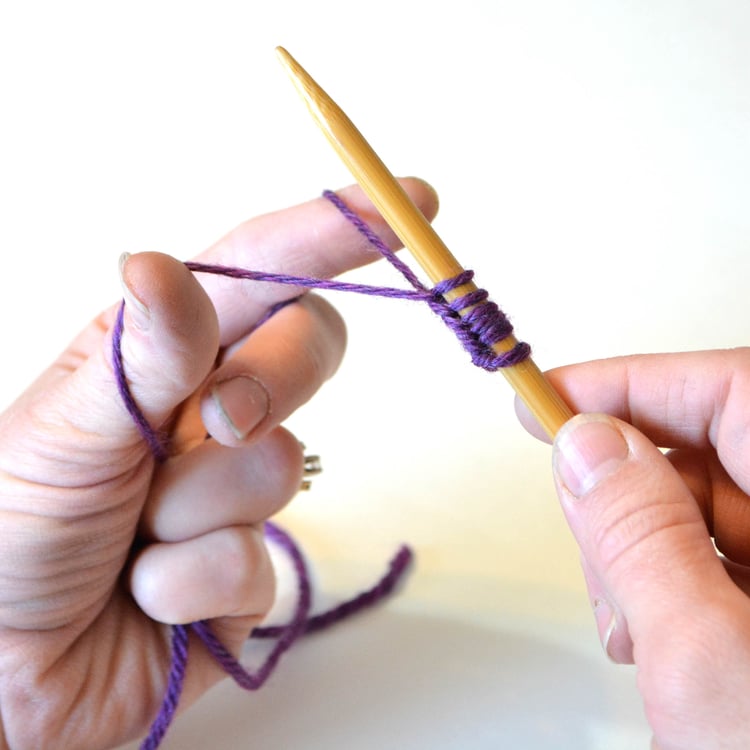 A pair of hands casting on stitches using two yarns.