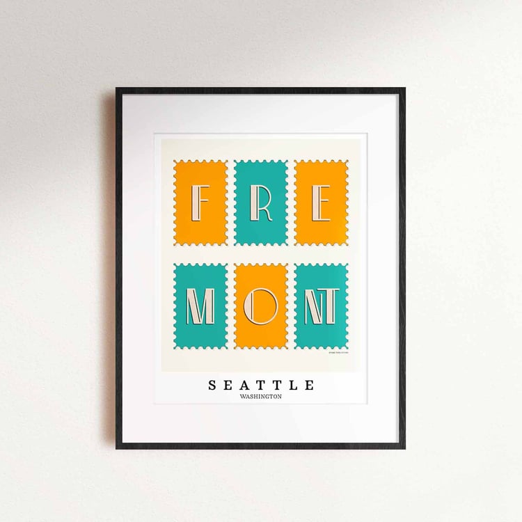 A framed picture of postage stamps featuring the Fremont neighborhood in Seattle, Washington drawn in a unique lettering style. Artwork has a bright blue and orange color scheme