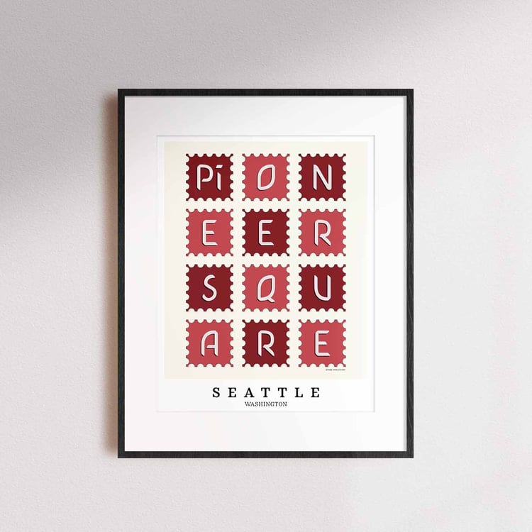 A framed picture of postage stamps featuring the Pioneer Square neighborhood in Seattle, Washington drawn in a unique lettering style. Artwork has a red and white color scheme
