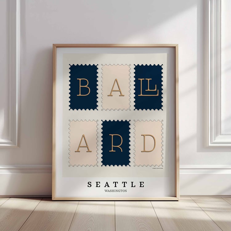 A framed picture of postage stamps featuring the Ballard neighborhood in Seattle, Washington drawn in a unique lettering style. Artwork has a navy blue, tan and beige color scheme
