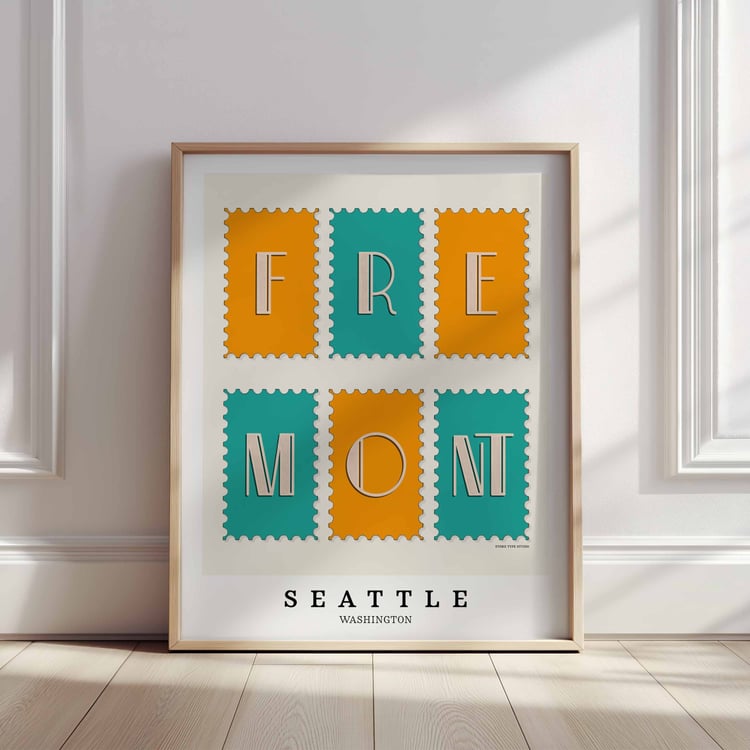 A framed picture of postage stamps featuring the Fremont neighborhood in Seattle, Washington drawn in a unique lettering style. Artwork has a bright blue and orange color scheme