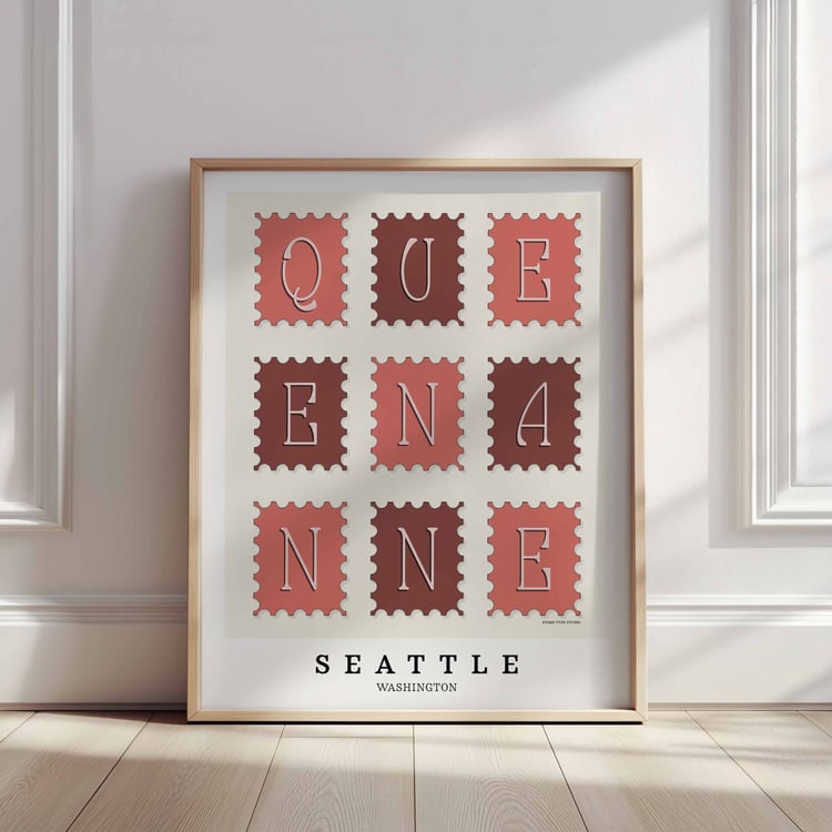 A framed picture of postage stamps featuring the Queen Anne neighborhood in Seattle, Washington drawn in a unique lettering style. Artwork has a pink, burgundy and white color scheme