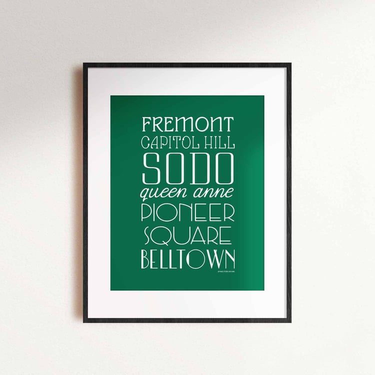 A framed picture of Seattle, Washington neighborhoods drawn in various lettering styles. Artwork has a green and white color scheme