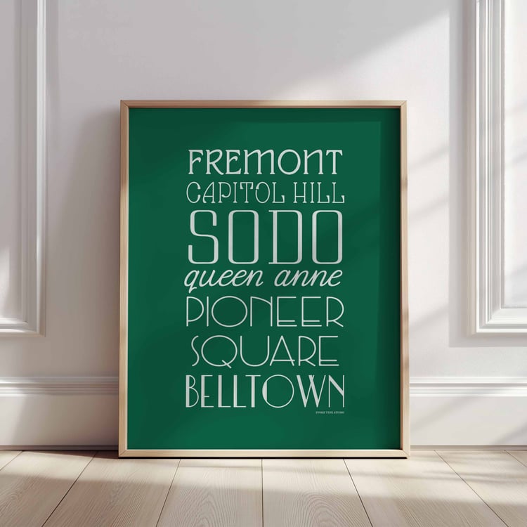 A framed picture of Seattle, Washington neighborhoods drawn in various lettering styles. Artwork has a green and white color scheme