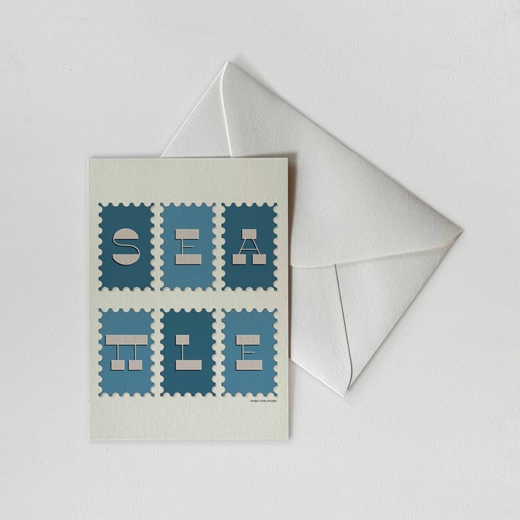 A notecard of postage stamps featuring Seattle, Washington drawn in a unique lettering style with a white envelope. Artwork has a blue and beige color scheme